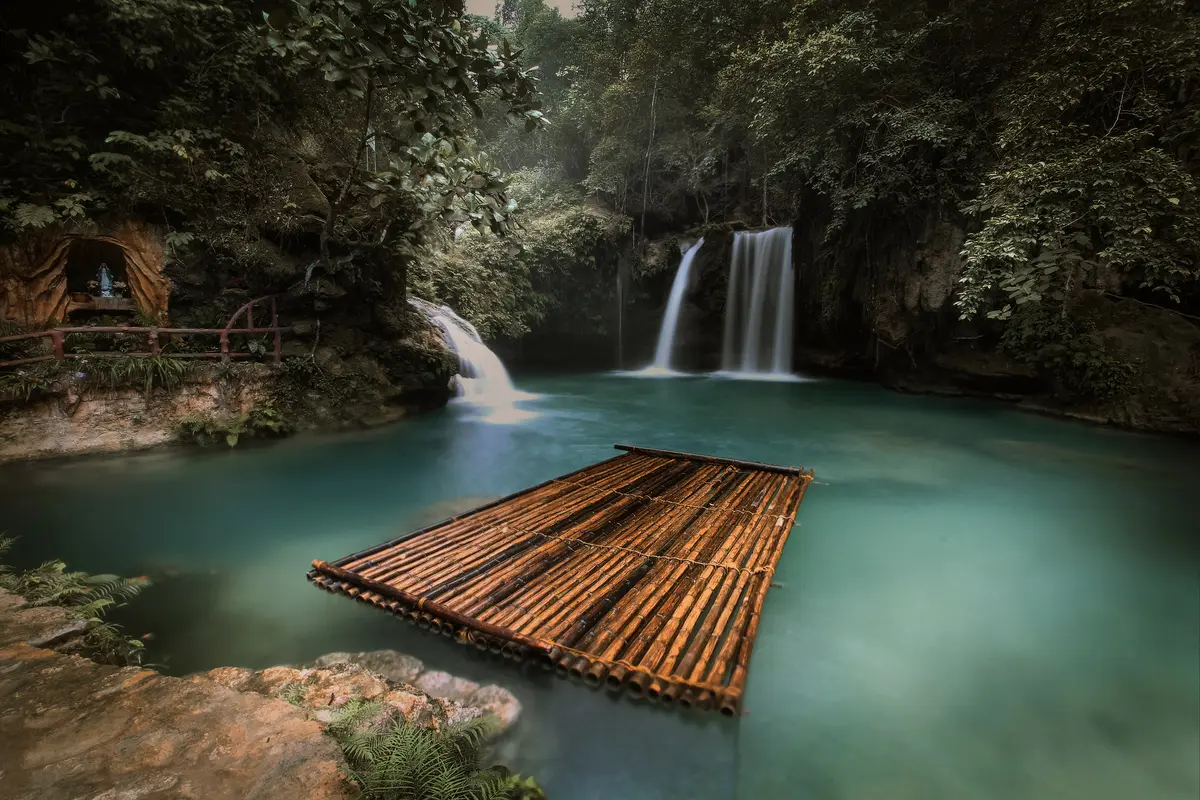 Kawasan Falls pouring into a turquoise pool with a bamboo raft