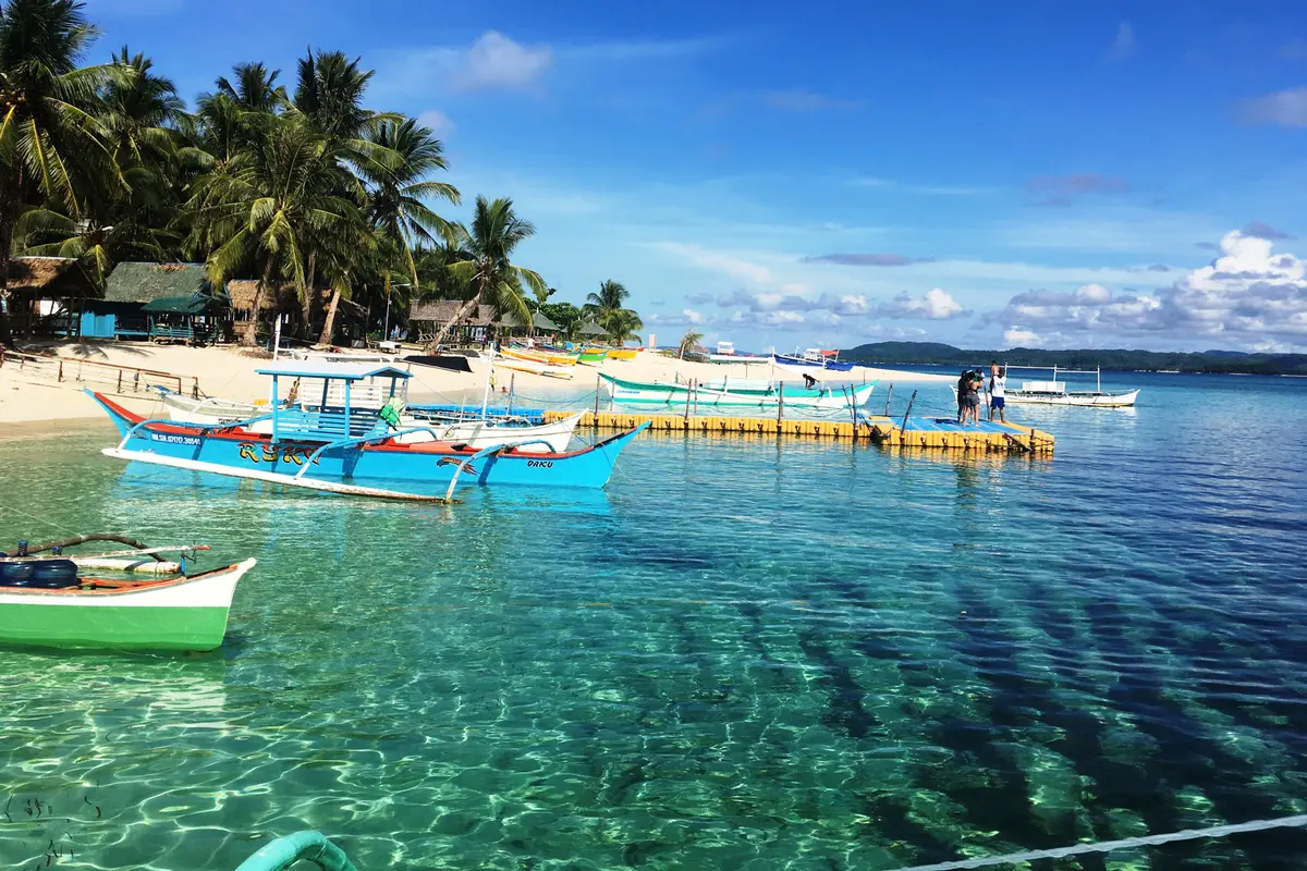 Outrigger boats moored in clear turquoise water below palm trees on Siargao