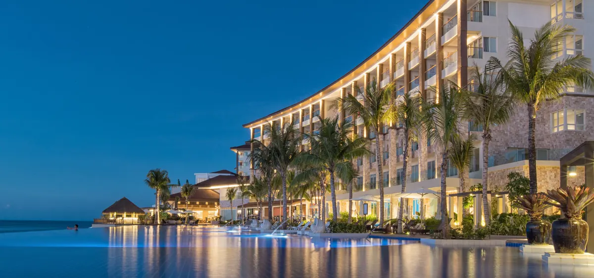 Dusit Thani Mactan Cebu at dusk, its curved building lit above the infinity pool